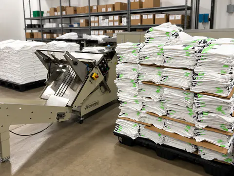 Automatic folding equipment beside organized stacks of printed shirts